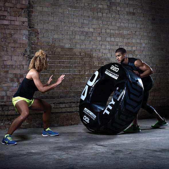 Training tyre in black with textured synthetic surface and integrated handles, shown in use; Inside Diameter 20"
